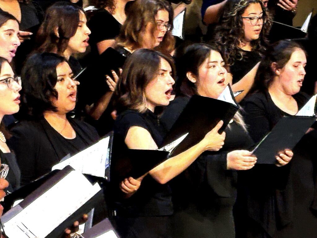 Singers performing in concert dress, holding black folders