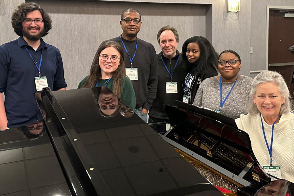 Directors and students gathered around a grand piano